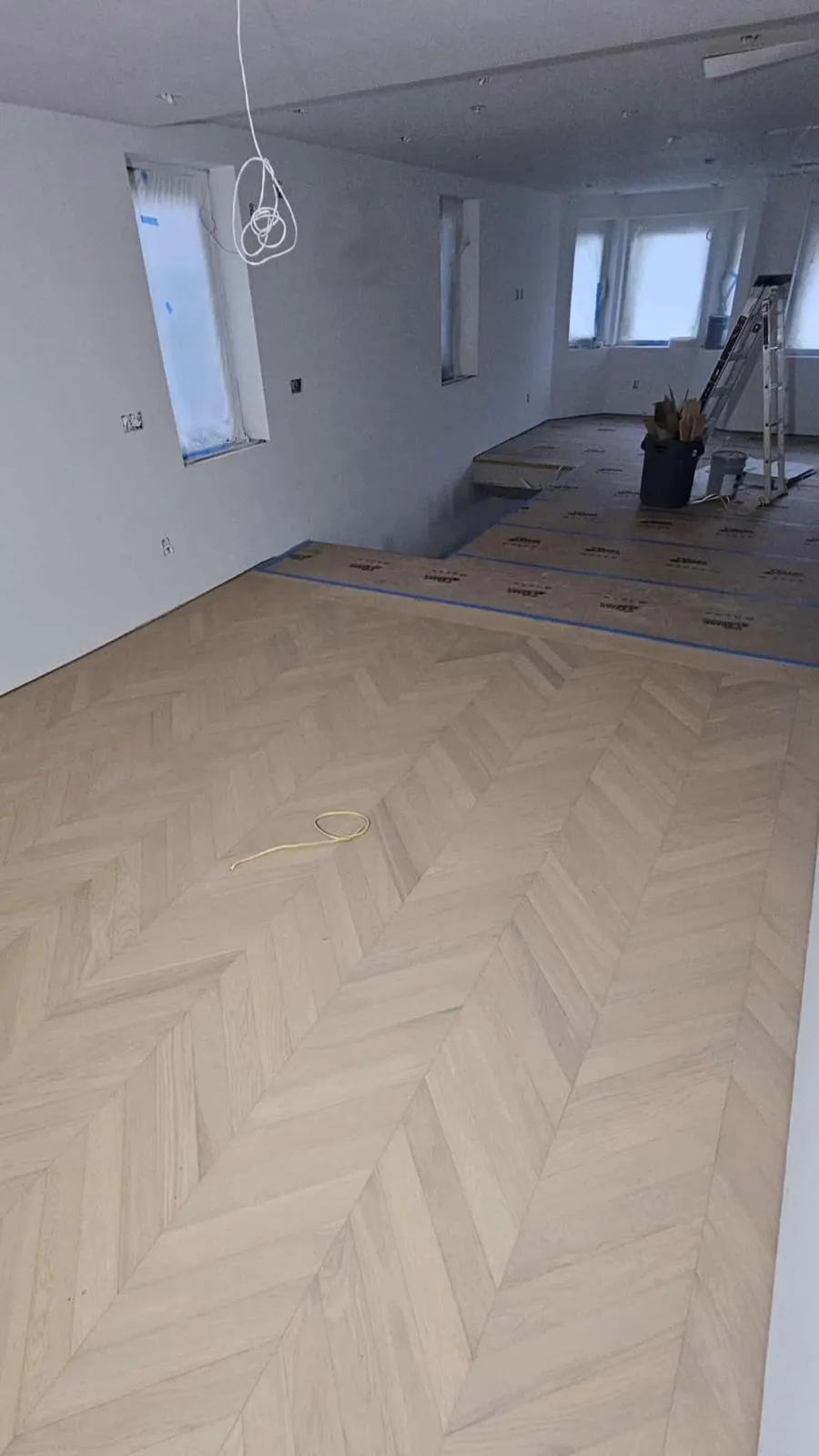 Empty room mid-project with a herringbone floor laid across it, a work light and a ladder against the far wall, in Leawood, Kansas